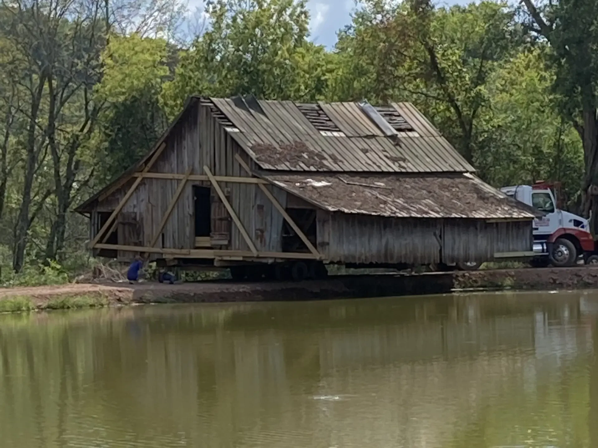 Barn being carefully transported by a lake.